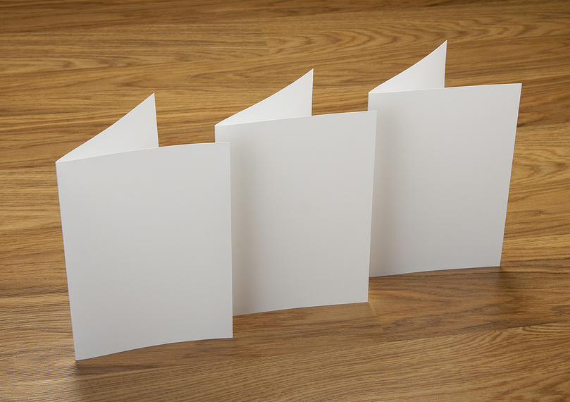 Three sheets of b-folded paper standing upright on a wooden table 