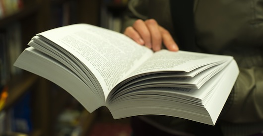 A person holding open a thick perfect bound book