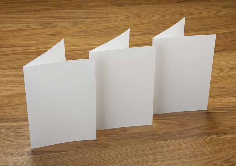 Three sheets of bi-folded paper standing upright on a wooden table