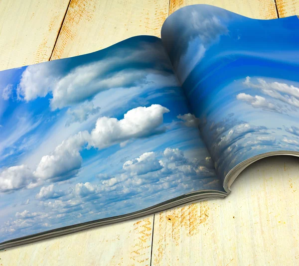 An open magazine printed with a picture of a blue sky with clouds that spans across two pages