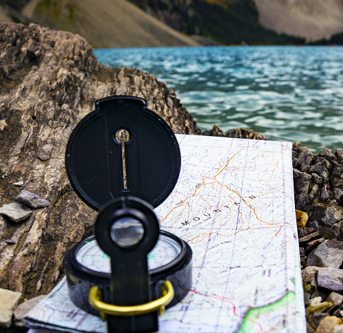 A folded map and a compass lying on rocks near a mountain stream 