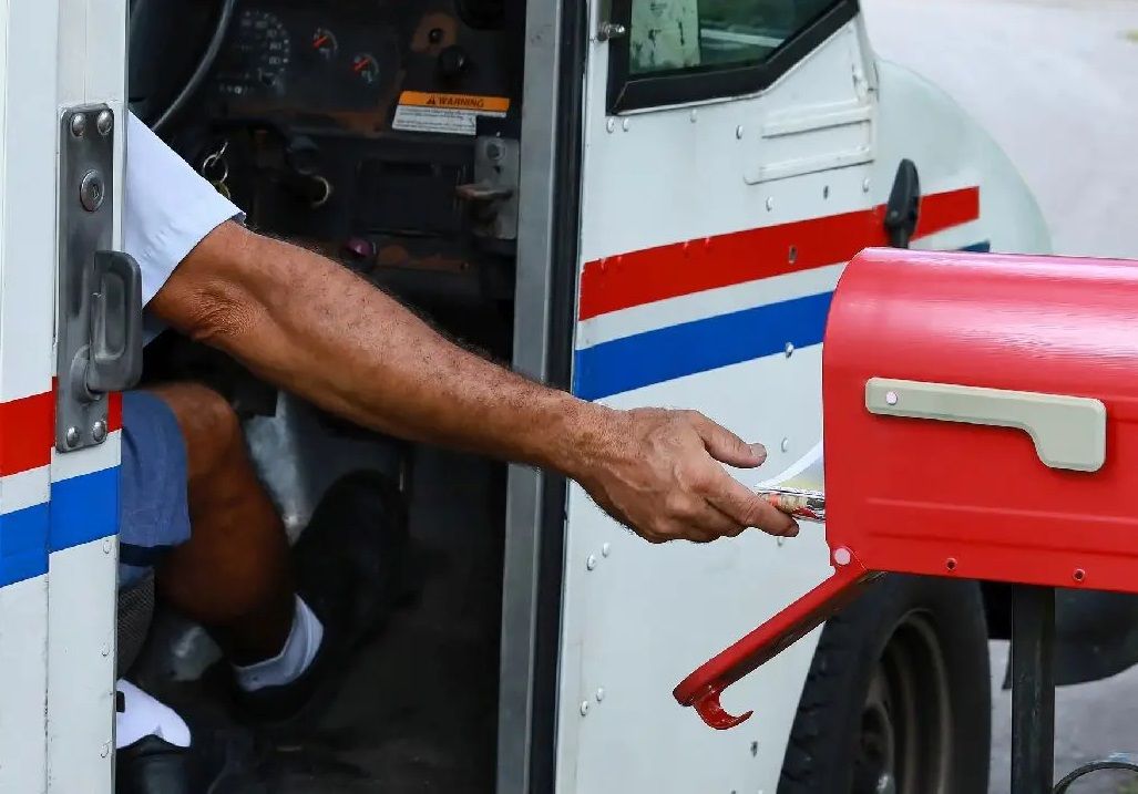 A mail carrier in a truck inserting mail into a mailbox