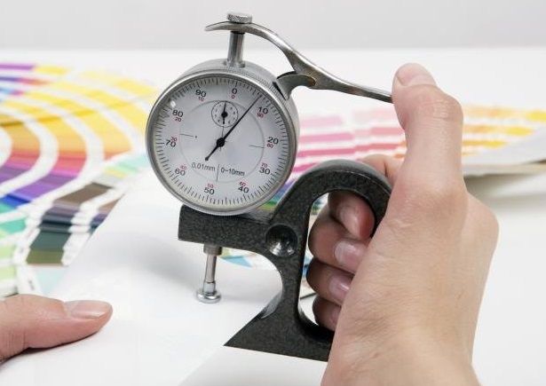 A man using a thickness gauge to measure a paper's caliper