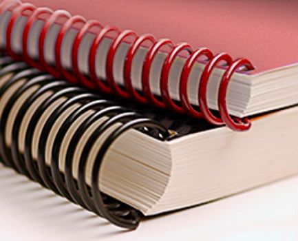 A red spiral bound book lying on top of a black spiral bound book