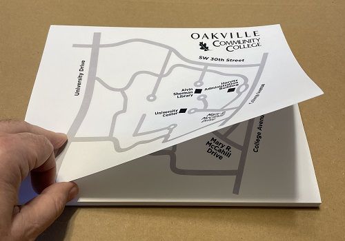 A hand lifting up the topmost sheet of a bound stack of grayscale maps