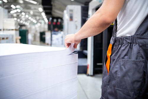 A print factory worker sifting through a stack of large paper sheets