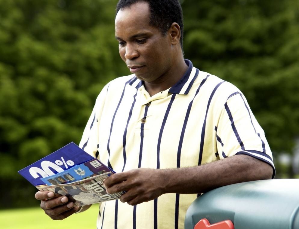 A postal customer reviewing direct mail pieces while standing by a mailbox