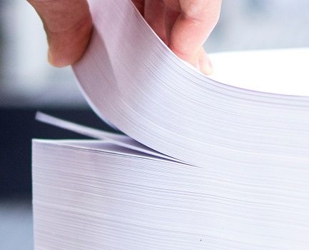 A hand lifting up some sheets from a large stack of white paper