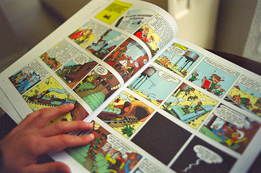 A hand holding open a printed comic book