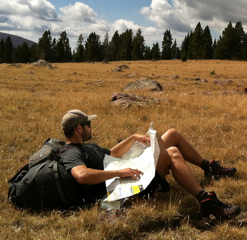 A hiker consulting a map while resting in a clearing
