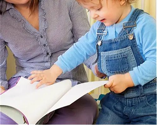 A young boy looks through a large book with his mother