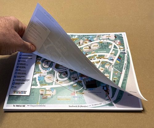 A hand lifting the topmost sheet from a stack of small printed maps