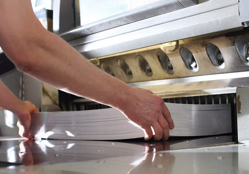 A worker placing a thick stack of sheets into a large paper shear