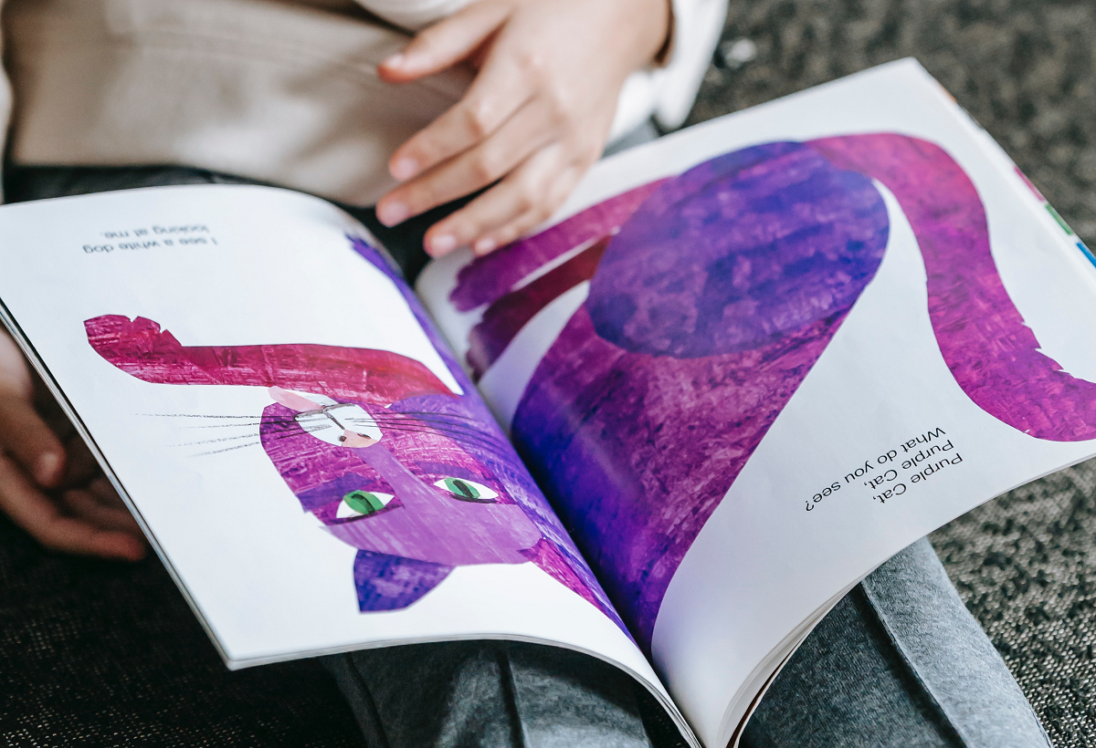 A child viewing a book that contains an illustration of a purple cat