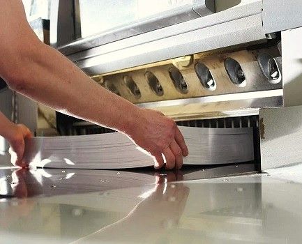 A print shop worker placing a thick stack of paper into a paper shear