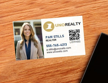 A business card for a female realtor lying on a desk next to a cell phone