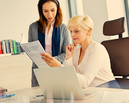 Two female office workers reviewing an Employee Handbook