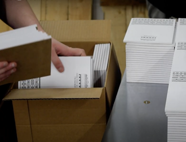 A printing plant worker packing a box with logo notepads