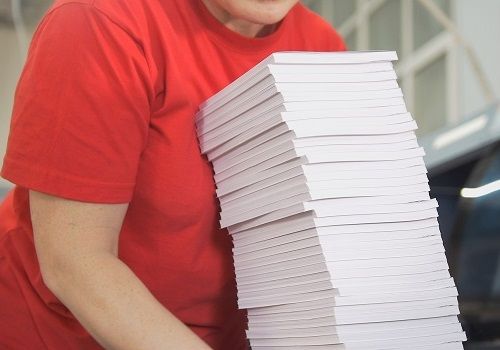 A printing plant worker carrying a tall stack of perfect bound books