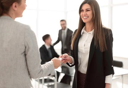 A young woman handing her business card to another woman