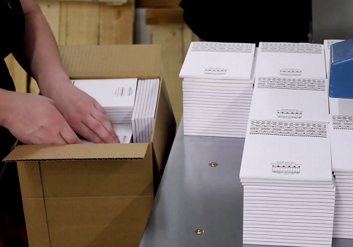 A worker at Color Vision Printing packing stacks of black and white notepads into a shipping box.