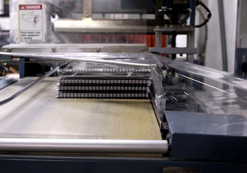 An industrial shrink-wrapping machine in Color Vision Printing's factory shown wrapping a stack of coil bound books in plastic prior to boxing and shipping.