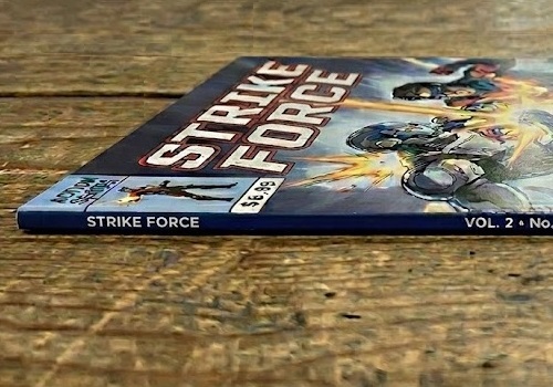 A perfect bound Strike Force comic book lying on a wooden surface