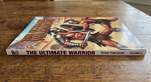 A perfect bound gladiator comic book entitled The Ultimate Warrior lying on a wooden tabletop