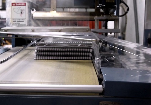 A stack of spiral bound books being processed through a Conflex shrink-wrapping machine prior to being boxed for shipping. 