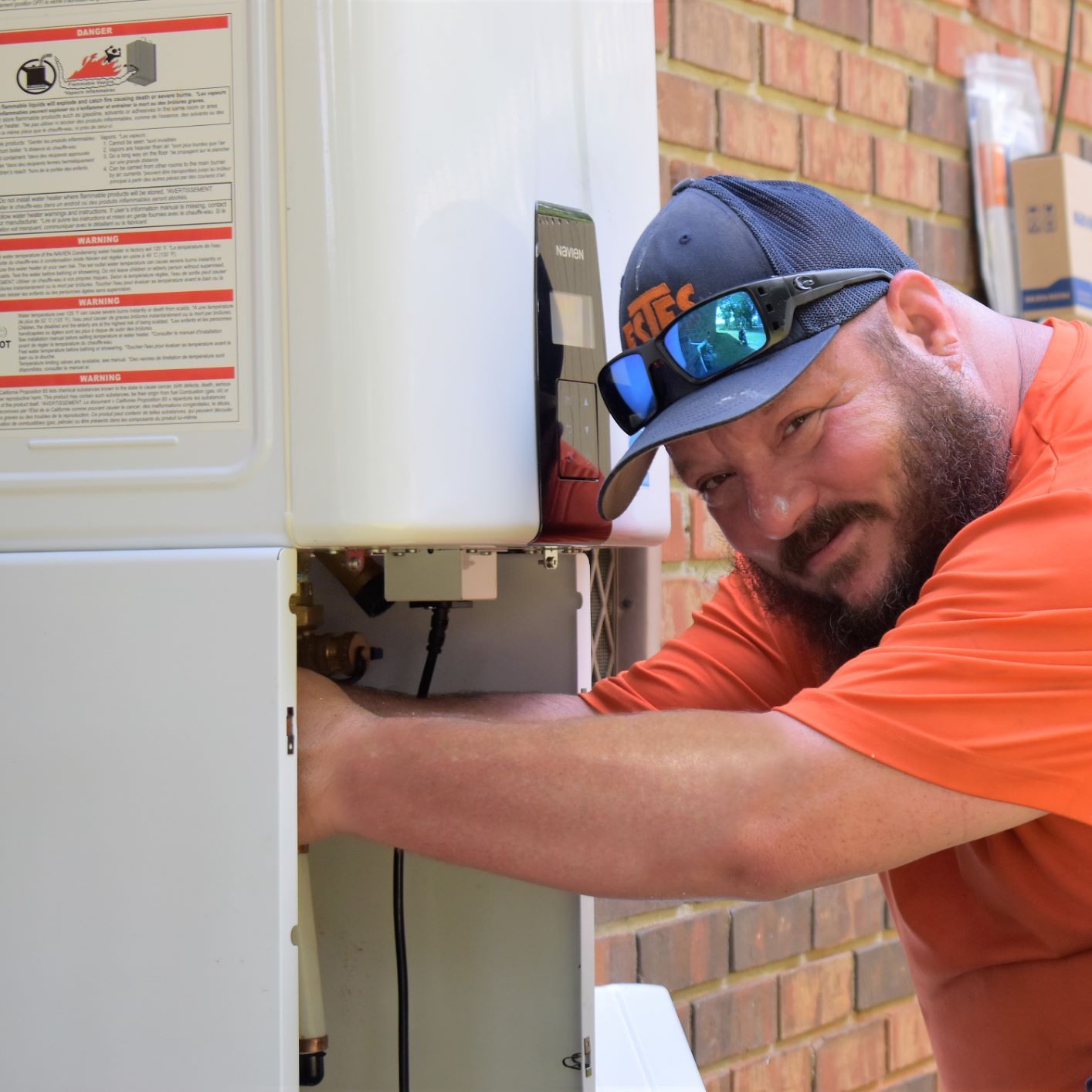 Estes Services plumber wearing an orange uniform and installing a tankless water heater