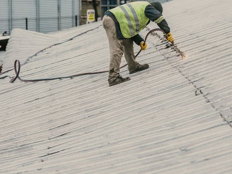 A man in a high-vis suit doing repairs on a roof.