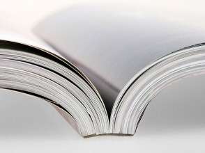 Close-up of an open magazine showing glossy pages and a curved spine on a white background