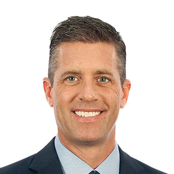 Smiling middle-aged man with short brown hair wearing a dark suit and light blue shirt on white background
