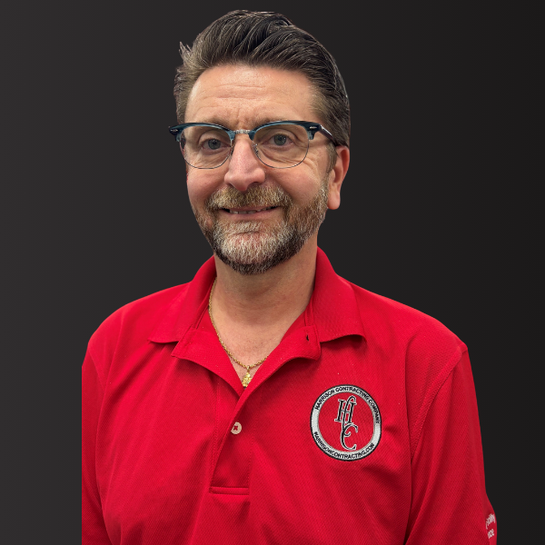 Smiling man with glasses and beard wearing red polo shirt with Henderson Contracting logo on black background