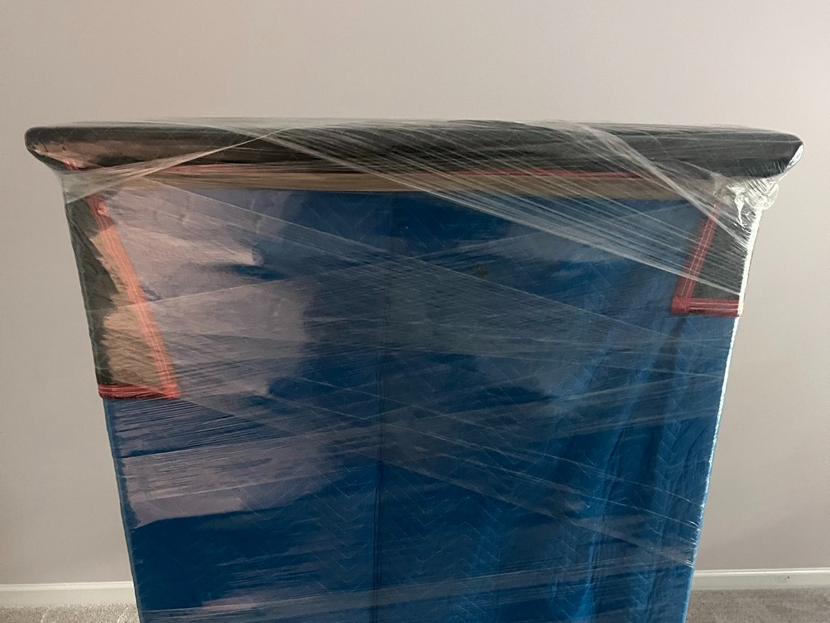 Blue furniture wrapped in protective plastic wrap standing on beige carpeted floor in a neutral room.