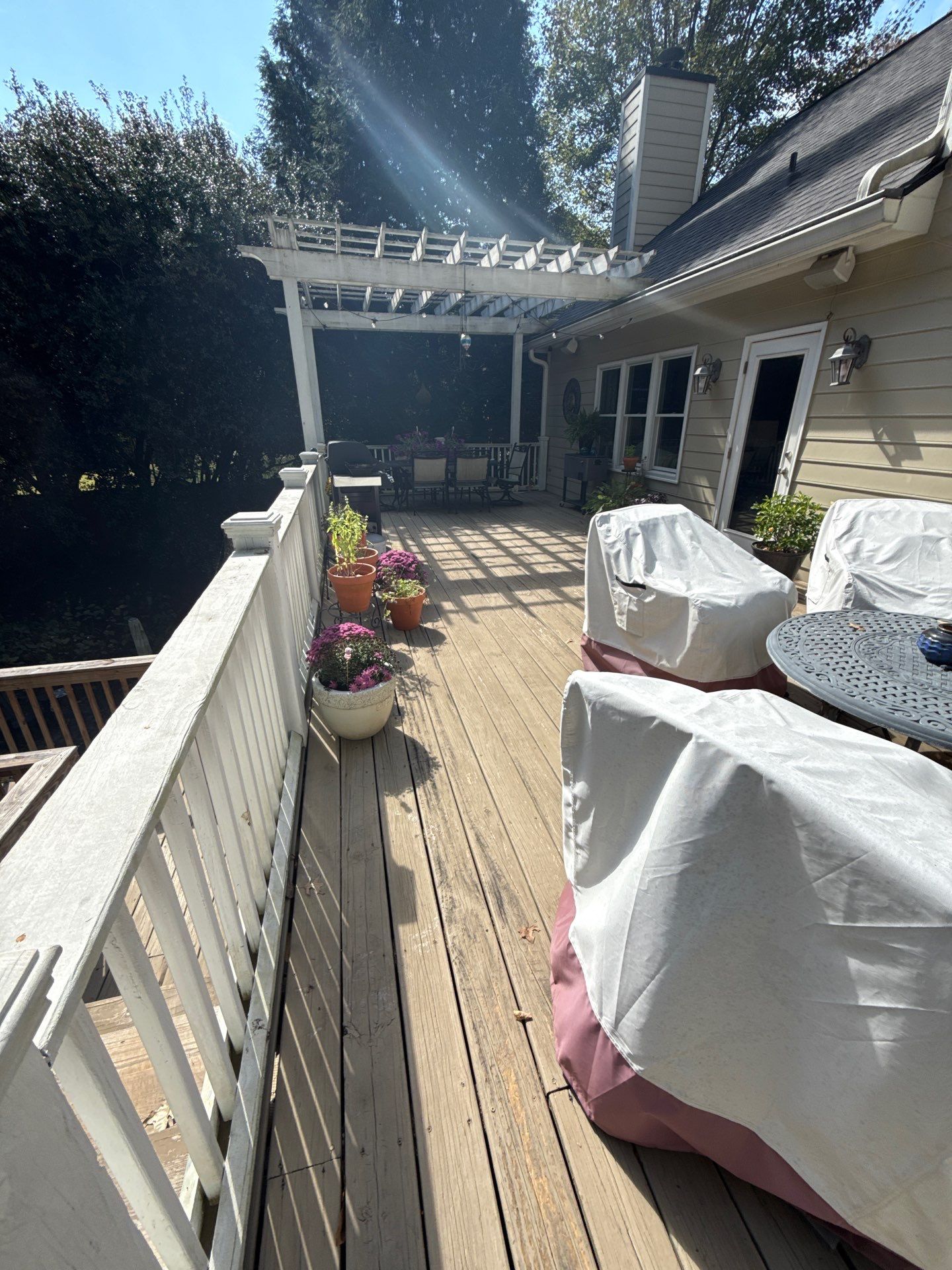 An outdated wooden backyard deck with weathered planks, a white painted railing, and an old pergola over the seating area prior to renovation by professional Marietta deck builders, deck remodeling in Marietta by Nelson Exteriors.
