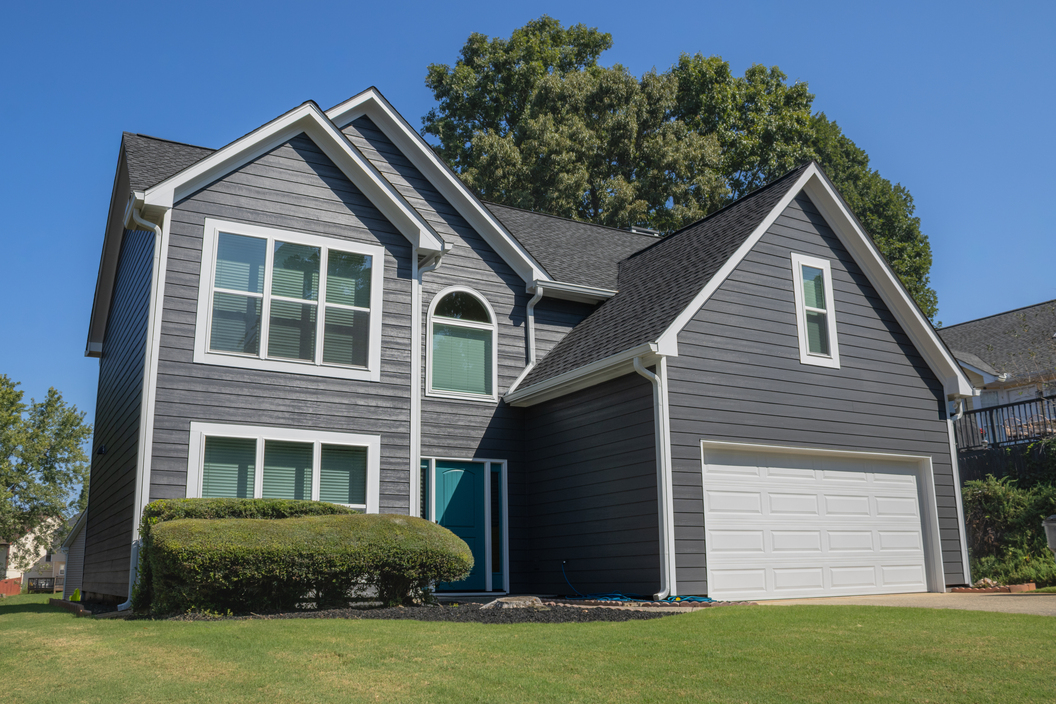 Modern two-story gray house with white trim, large windows, a green lawn, and attached garage under a clear sky.