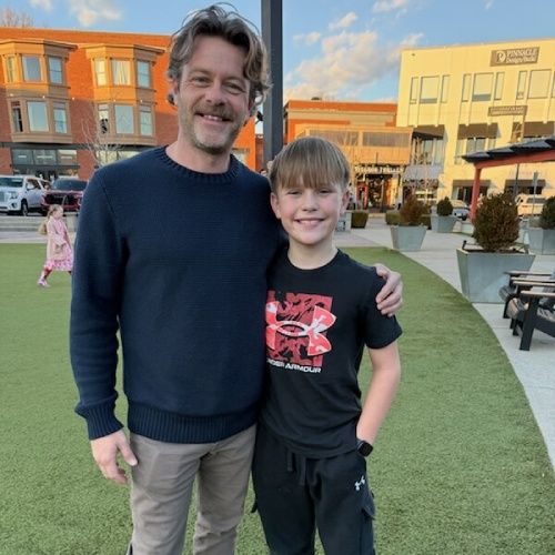 Josh Motes of Nelson Exteriors standing outdoors with a child at a town center