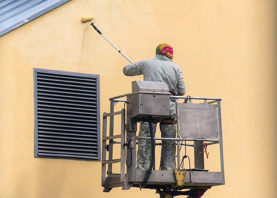 man rolling paint on exterior of home