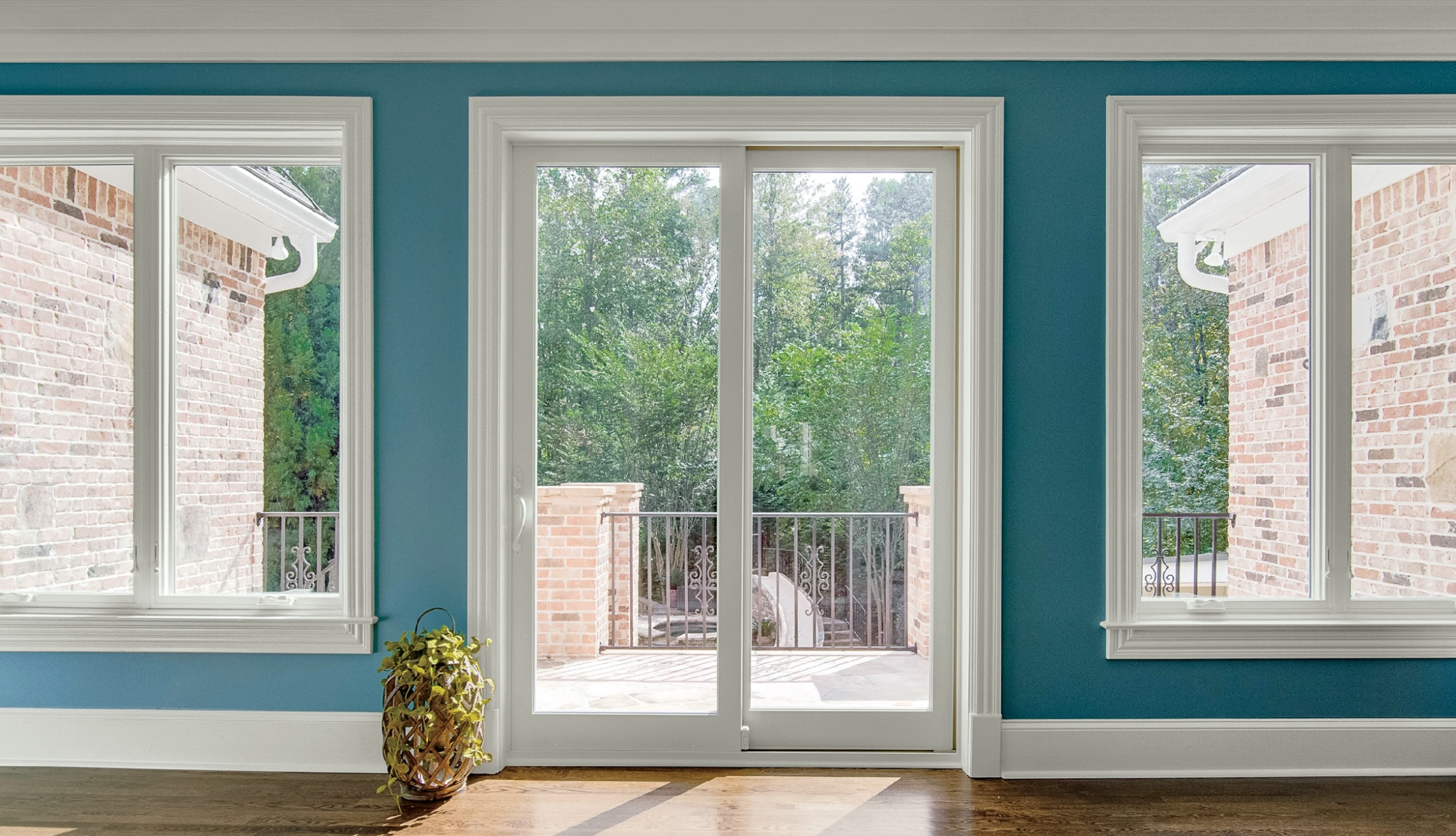 Interior view of blue room with white trim, hardwood floors, Infinity windows, Infinity from Marvin Sliding French Doors looking out onto balcony of brick house with trees in the background