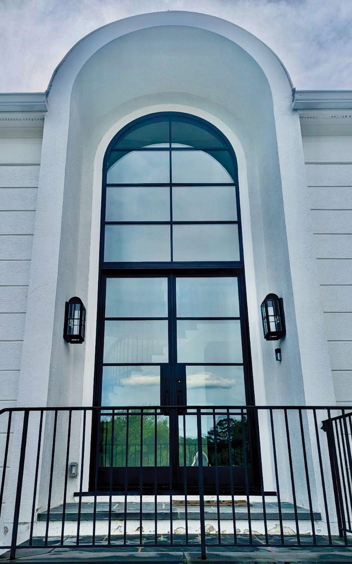 Iron entry double door with arched iron foyer window above it.