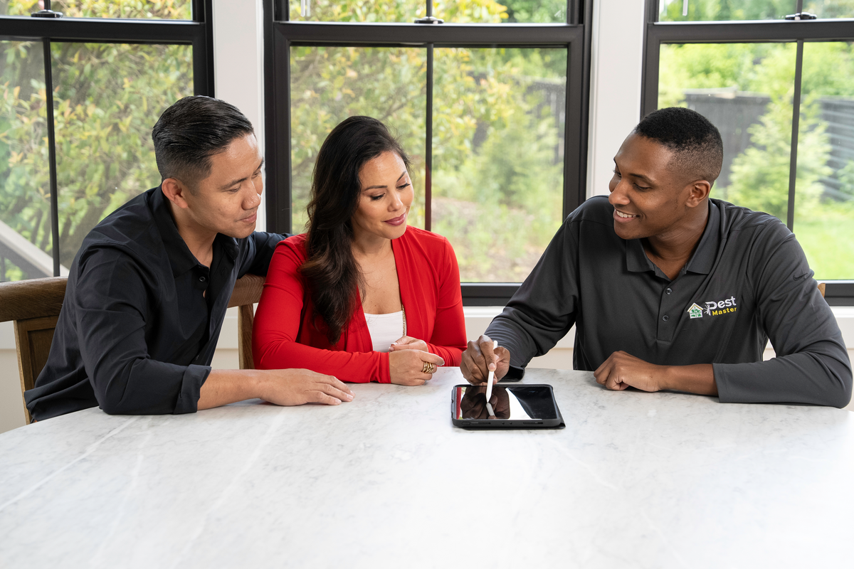 est control expert using tablet to explain service details to a couple at a white marble table by window.
