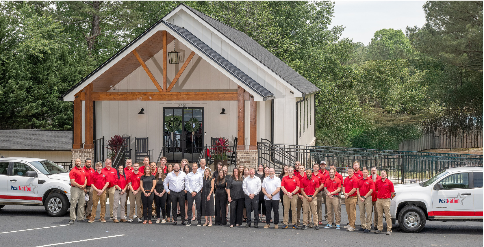 PestNation team in red and black uniforms posing outside a modern office building with company trucks parked nearby