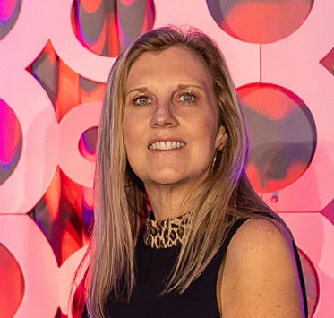 Kim Gubera in black top with leopard print collar against a pink and orange abstract geometric background