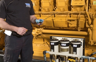 Technician inspecting large yellow industrial engine with blue cloth in hand and equipment in foreground.
