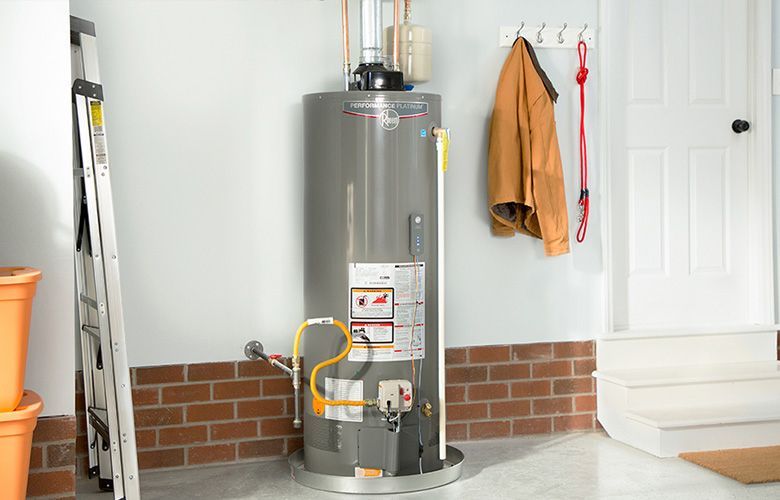 Modern gray water heater installed in clean basement with brick wall and hanging coat.