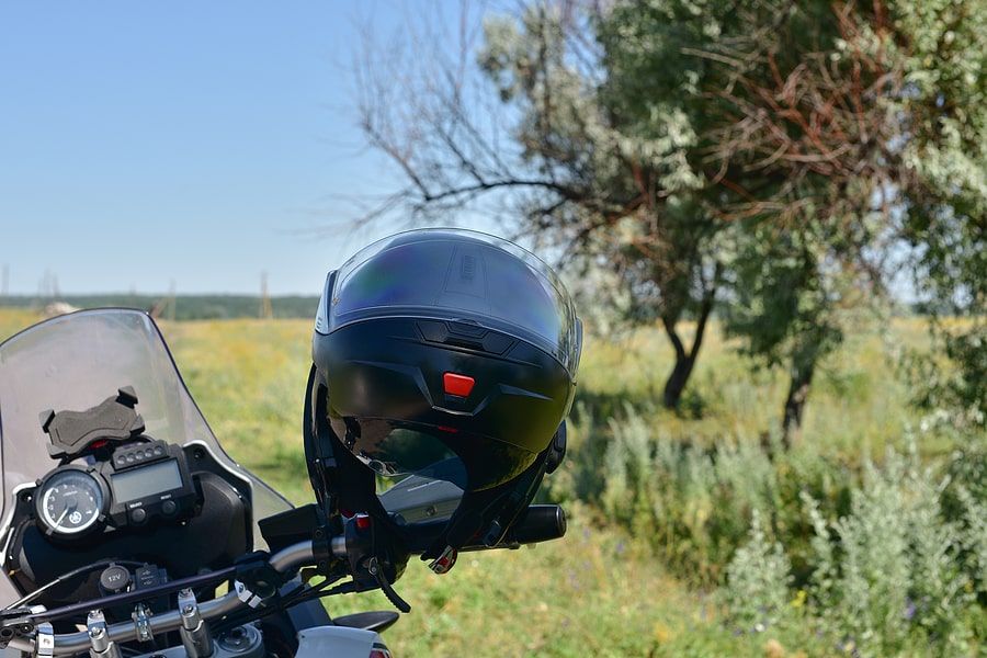 Close up of a motorcycle parked next to a field with a helmet on the arm