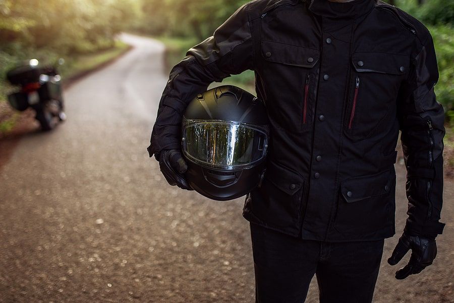 Person dressed in all black walking down the road with a helmet in hand