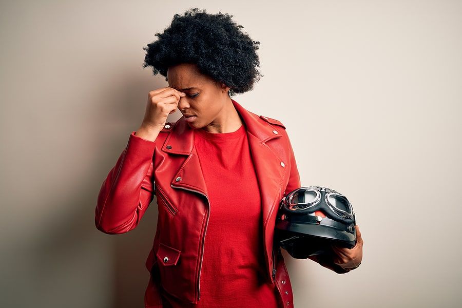 Black woman holding her head in concern with a helmet in her hand 