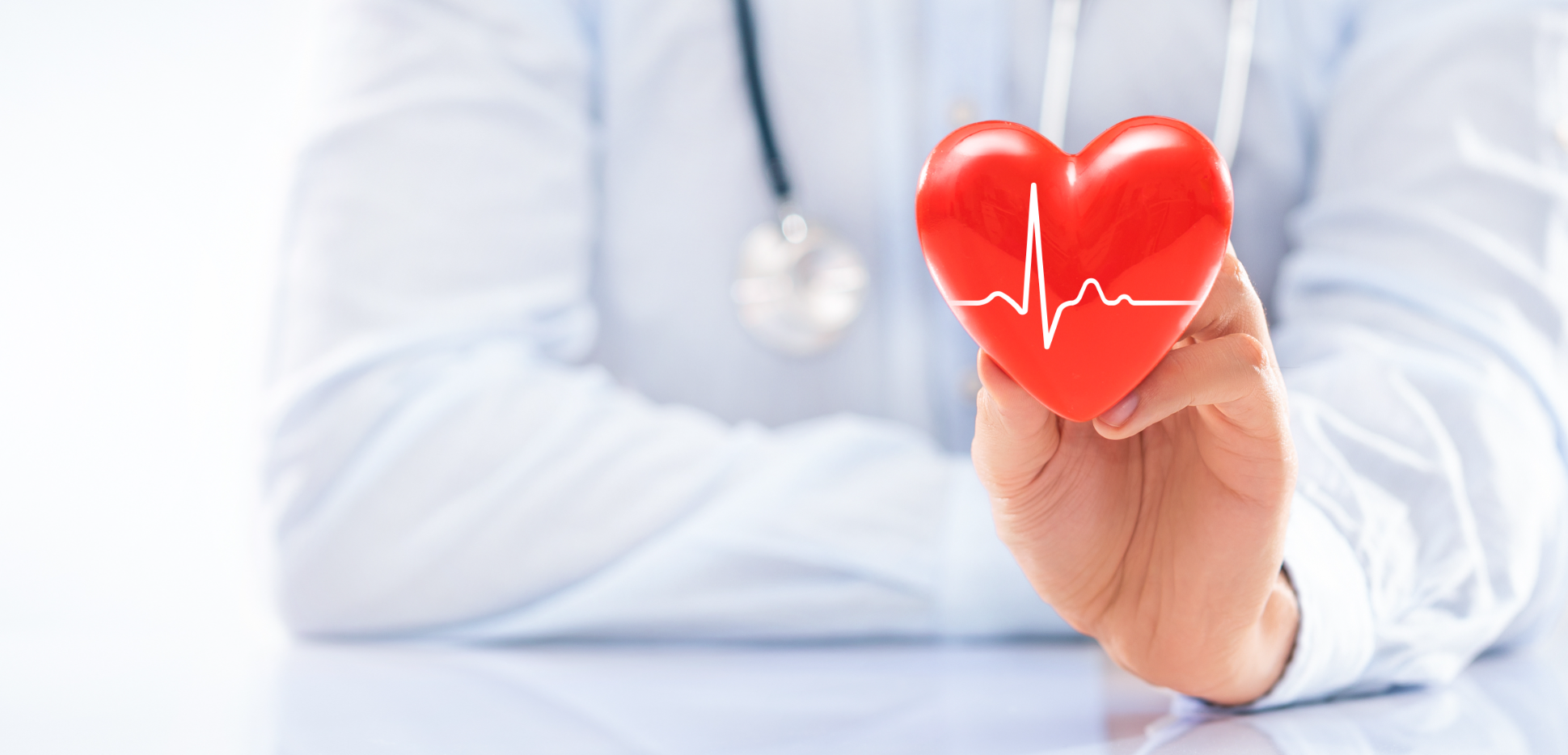 Close-up of a doctor's arms holding a red heart with an EKG line across it